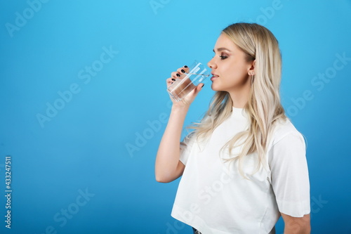 young woman drinking water on blue background. girl holding a glass of water