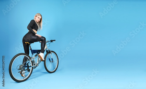 studio shot of a sportive woman sitting on a bicycle on blue background with copy space. beautiful young woman wearing sportswear posing with a bike in a photo studio