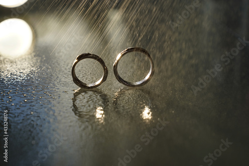 two wedding gold rings reflected in the mirrored surface under the water drops