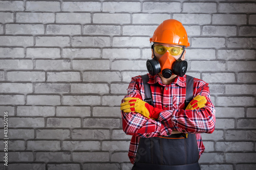  Man wearing helmet, gloves glasses, protective gear near brick wall with copy space. Work safety concept.