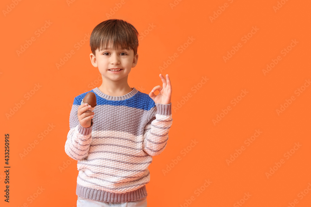 Cute little boy with chocolate Easter egg showing OK on color background