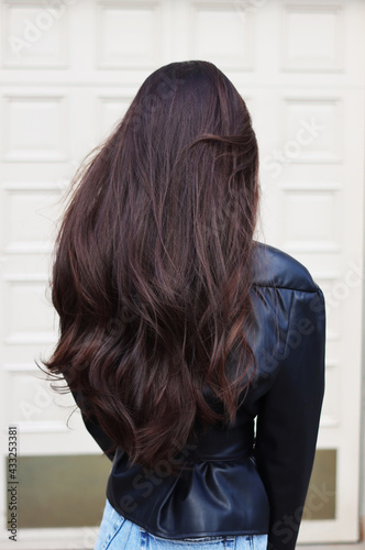 Long, thick, dark natural hair. Hairstyle. Loose strands lie in beautiful waves. Portrait of a Caucasian lady from the back