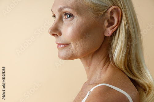 Close up portrait of mature blonde woman in white underwear looking away, posing isolated over beige background