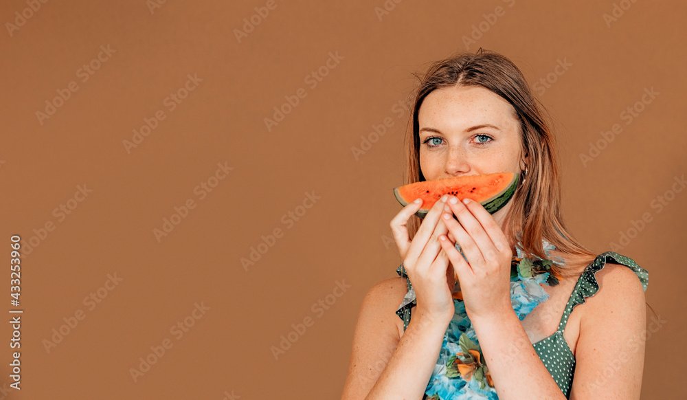 smiling caucasian girl holding slice of watermelon in front her mouth on brown background with copyspace. smiling caucasian girl holding slice of watermelon in front her mouth on brown background with copyspace.