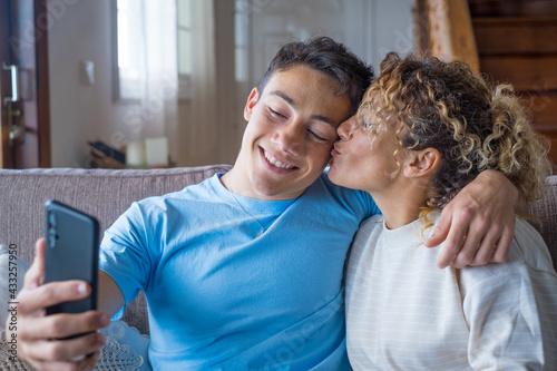 Smiling middle-aged 40s mother rest with grown-up son using smartphone together, happy young man enjoy family weekend with mom browsing wireless Internet on cellphone, have fun at home 