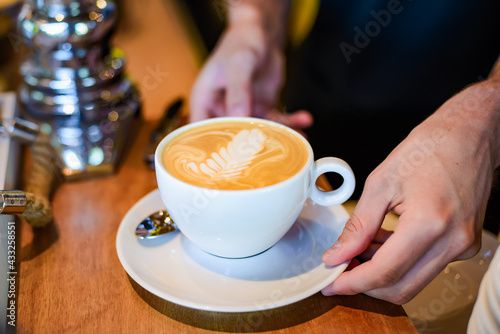 Hands putting fresh made coffee cappuccino on brown wood table
