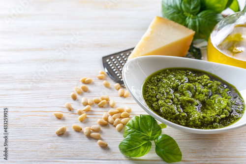 Homemade pesto sauсe with ingredients. Sauсe pesto in white bowl with basil, olive oil, pine nuts and parmesan cheese on white wooden background with copy space for text.