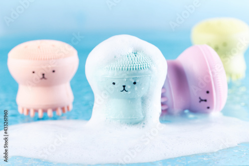 Silicone massage brushes for washing with funny faces in water covered with foam. Marine mood and freshness. Water treatments and SPA concept