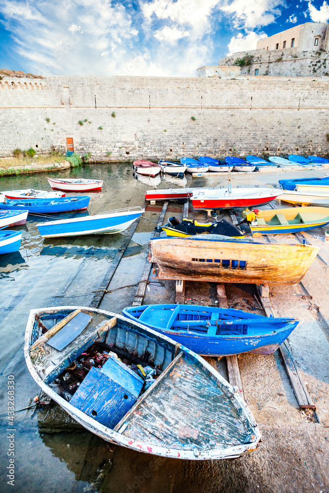 Old colored wooden boats in the small harbor near the Angevin castle in Gallipoli. Old and worn colored boats on the shore of the sea of Gallipoli in Italy. Blue sky with clouds.