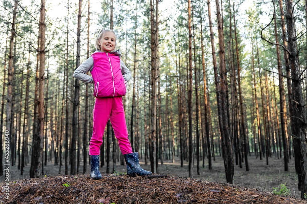 Cute pretty blond caucasian happy child funny girl in bright pink suit enjoy walking in wet coniferous pine forest on sunny morning day. Little female kid portrait hiking nature trip outdoors Cute pretty blond caucasian happy child funny girl in bright pink suit enjoy walking in wet coniferous pine forest on sunny morning day. Little female kid portrait hiking nature trip outdoors
