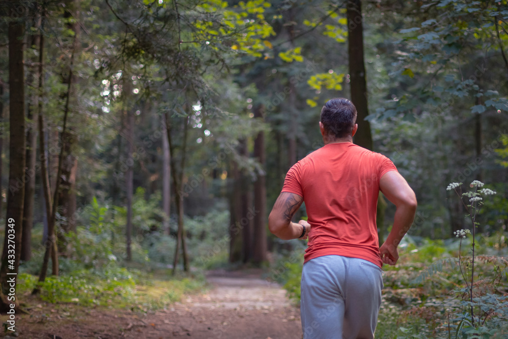 Back view of a Caucasian man in sportswear running along a forest trail, close up