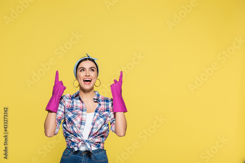 Positive housewife in pink rubber gloves pointing with fingers isolated on yellow