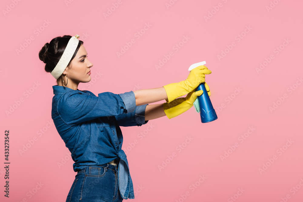 Side view of housewife holding detergent and rag isolated on pink Side view of housewife holding detergent and rag isolated on pink