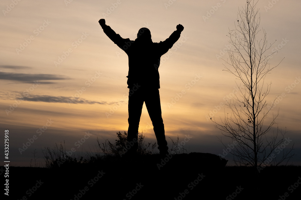 silhouette of a winner man throwing his hands up standing on a mountain