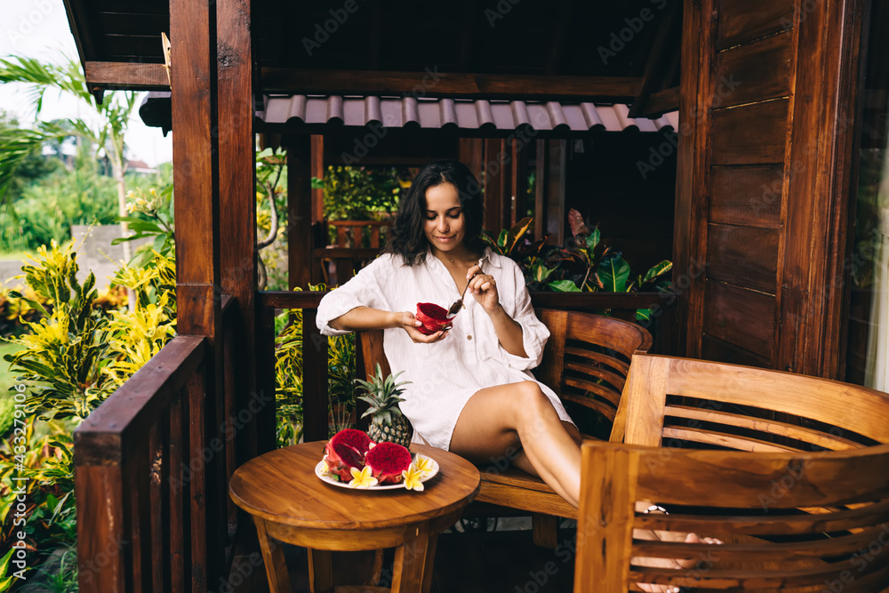 Glad woman eating exotic fruits on porch in countryside house