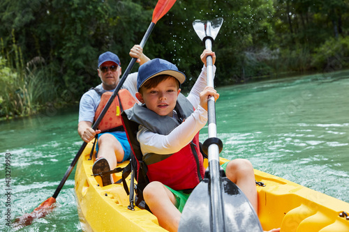 Cute boy and father canoeing in lake during vacation photo