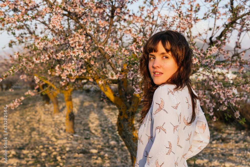 Young woman looking over shoulder at almond trees during sunset Young woman looking over shoulder at almond trees during sunset