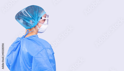 Profile photo of a female doctor in a coat, goggles and a mask. The doctor fights the spread of the covid 19 virus. Gray background and side space.