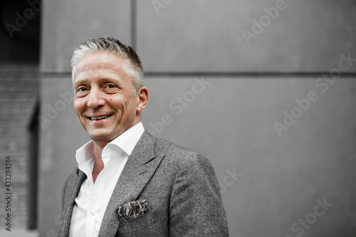 Smiling well-dressed male investor in front of gray wall