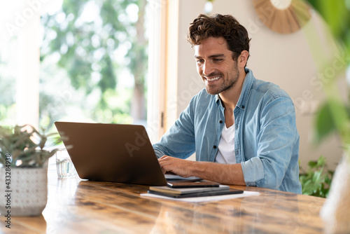 Smiling freelance worker using laptop while sitting at table photo