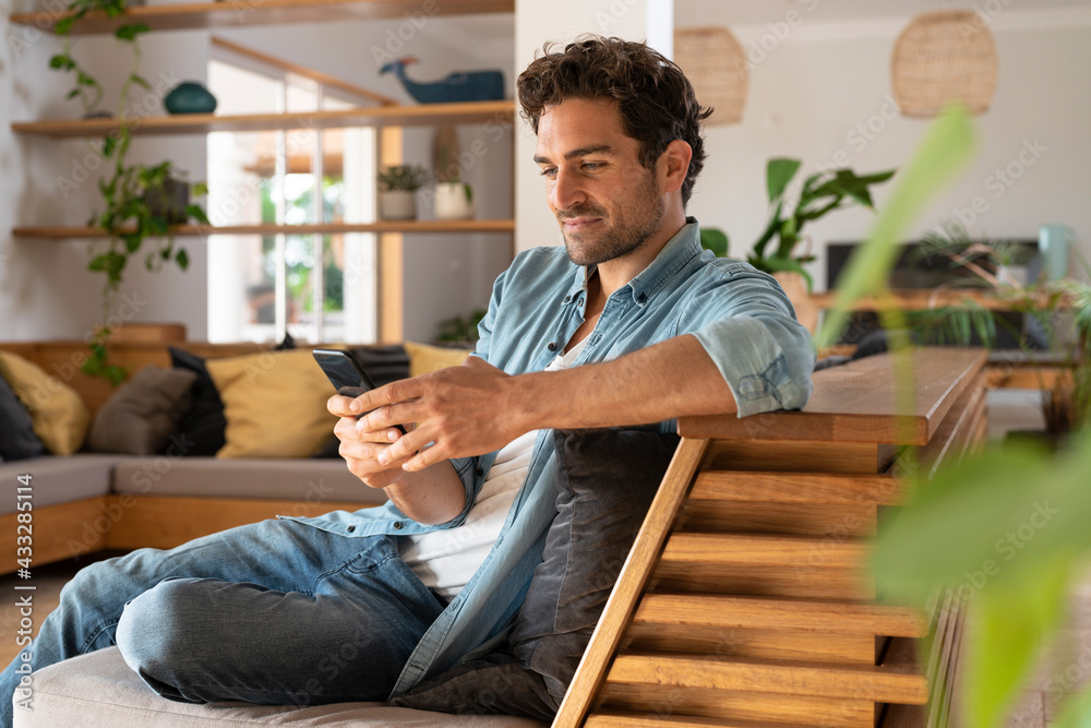 © steve brookland/Westend61 - Man using mobile phone while sitting on sofa at home © steve brookland/Westend61 - Man using mobile phone while sitting on sofa at home