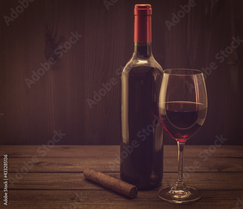 Bottle of red wine with a glass of red wine and cuban cigar on an old wooden table