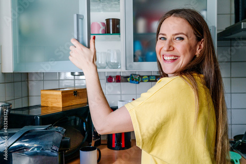 Happy woman with gray eyes opening door of cabinet in kitchen at home photo