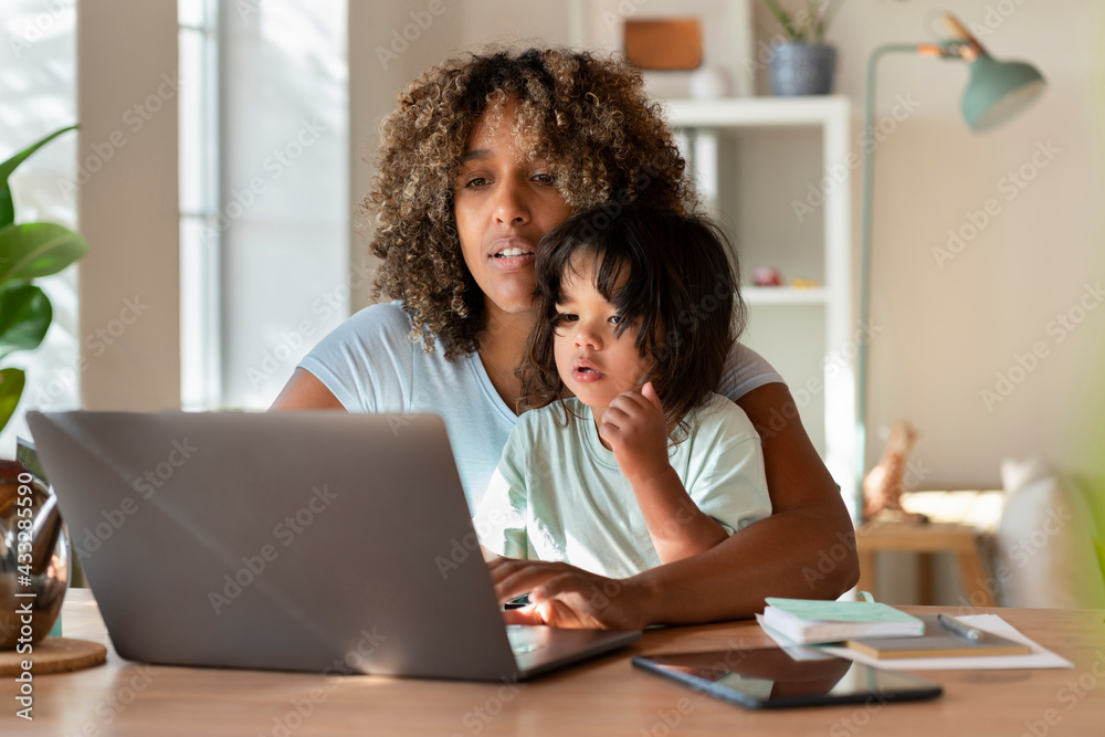 Mother and toddler daughter looking at laptop together while working from home Mother and toddler daughter looking at laptop together while working from home