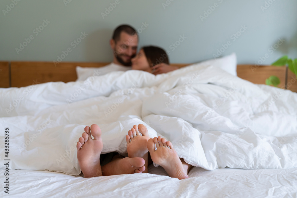 Happy couple with white sheet cuddling on bed in bedroom at home Happy couple with white sheet cuddling on bed in bedroom at home