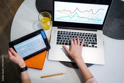 Woman doing calculation on digital tablet while working on graph on laptop at home photo