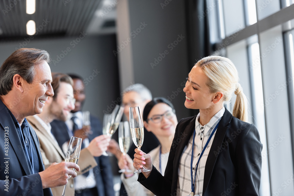 smiling interracial business people holding champagne glasses during conversation in hall smiling interracial business people holding champagne glasses during conversation in hall