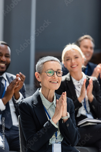 selective focus of middle aged businesswoman applauding near interracial colleagues on conference