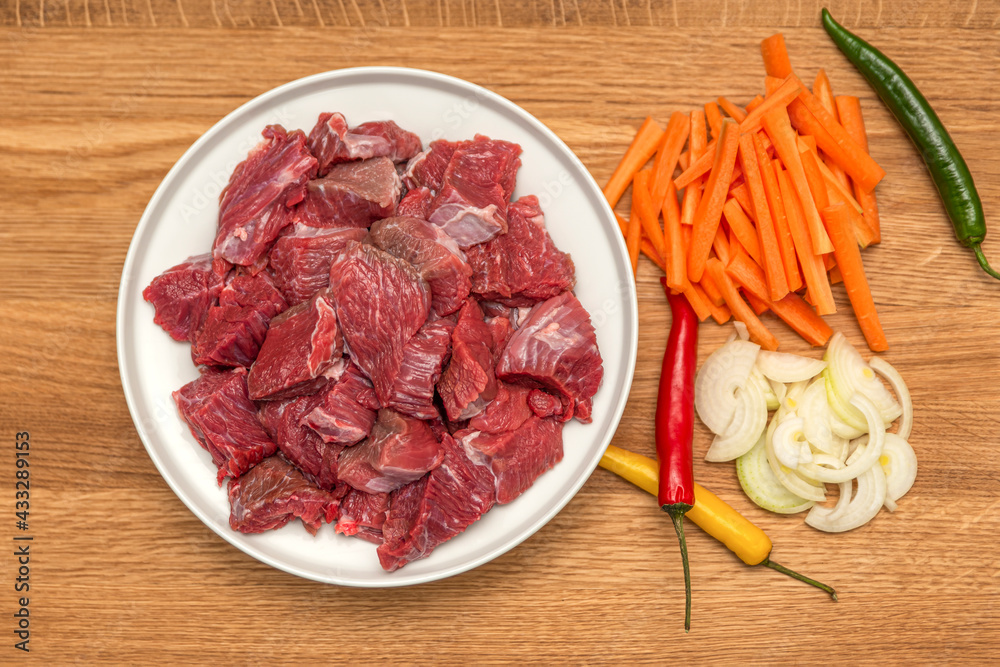 Ingredients for cooking pilaf on a wooden background. Onions, peppers, carrots, minced meat lie on a wooden cutting board. Cooking pilaf at home