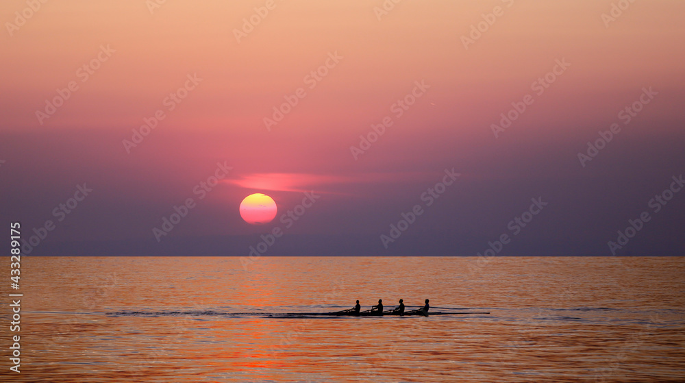 People silhouettes on rowing boat in front of sunset background. Front view