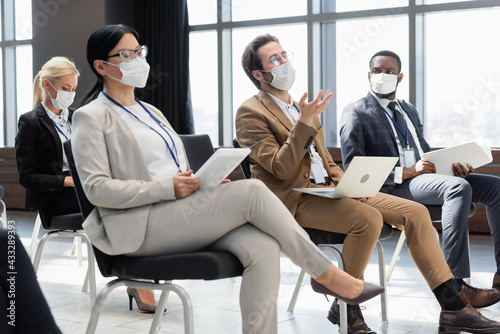 young businessman pointing with hand near interracial colleague in medical masks