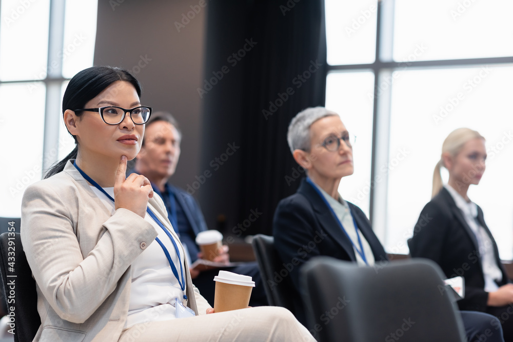Asian businesswoman with coffee to go sitting in conference room near colleagues Asian businesswoman with coffee to go sitting in conference room near colleagues