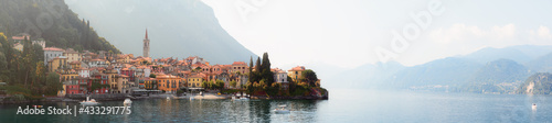 Early morning view of the Como Lake with the village of Varenna, Italy, and clear sky, with fog, soft sunlight and mountains in the distance