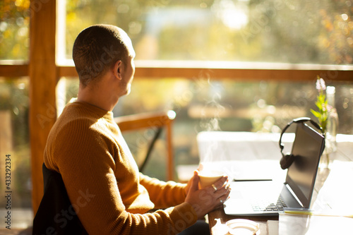 Thoughtful businessman with coffee and laptop looking out sunny window