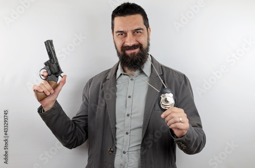 Detective with beard smiling showing police badge holds the gun with his arm up. Crime concept.
