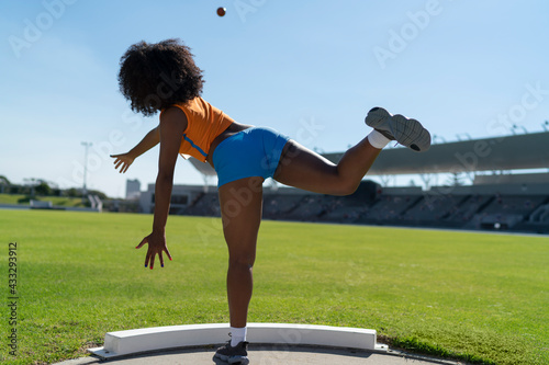Female track and field athlete throwing shot put in sunny infield