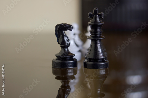 Black horse chess and black king chess stand encounter on a chessboard against white pawn. Chess piece icon macro closeup shot.