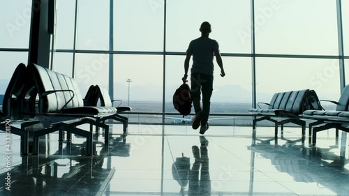 People at the airport lounge ready for the holiday, running, positive emotions. Man with backpack jumping near the window at empty during Covid lockdown airport. Celebrating