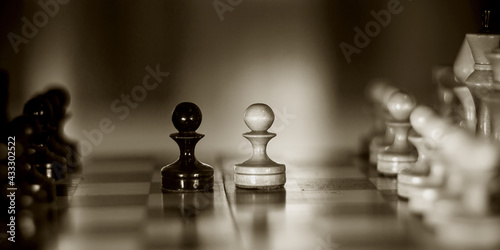 Two chess pieces are pawns  black and white. Wooden chess pieces on the chessboard.