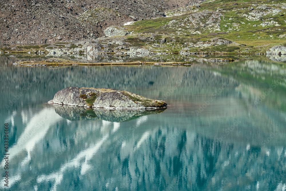 Fototapeta premium Rock in turquoise mountain lake. Snowy mountain reflected in azure clear water of glacial lake. Beautiful sunny background with snow-white glacier reflection in green water surface of mountain lake.