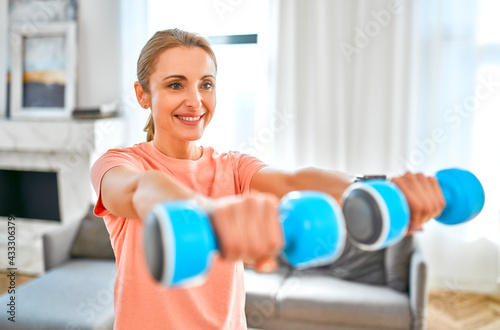 Sport, fitness and healthy lifestyle concept. Mature woman doing exercises with dumbbells at home. How to stay healthy in quarantine.