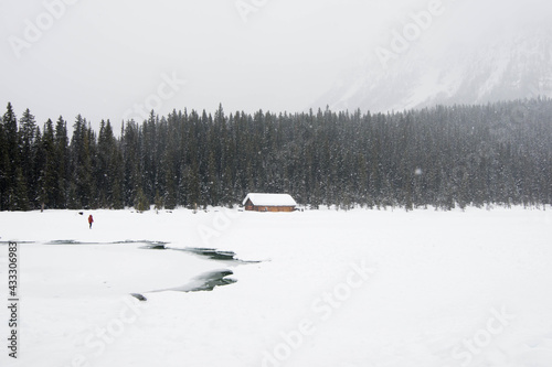 One person dressed in red in a winter landscape. Frozen lake, wooden house and a forest under the snow. Banff National Park, Alberta, Canada