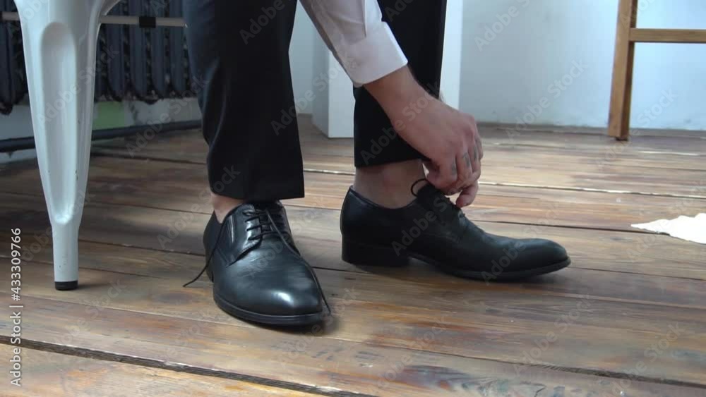 Slow Motion Man ties the laces on black shoes. Close-up of hands and shoes