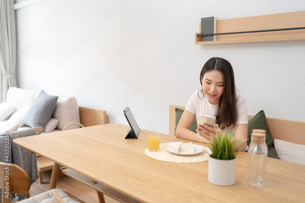 Happy asian woman using mobile phone during breakfast or eating lunch while working from home. Happy asian woman using mobile phone during breakfast or eating lunch while working from home.