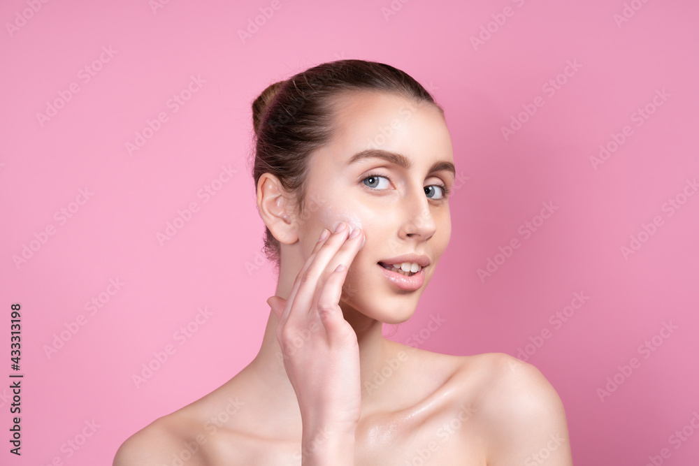 Beautiful young woman applying cream on her face against color background Beautiful young woman applying cream on her face against color background