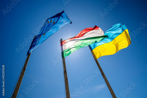 Flags of Hungary Ukraine and European Union waving on pole against blue sky